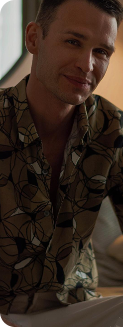 Mężczyzna w kolorowej koszuli siedzi i lekko się uśmiecha, patrząc w stronę aparatu.