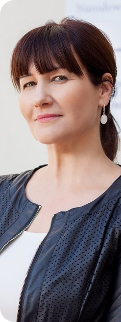 Kobieta z ciemnymi włosami pozuje w czarnej kurtce, patrząc pewnie w stronę obiektywu.