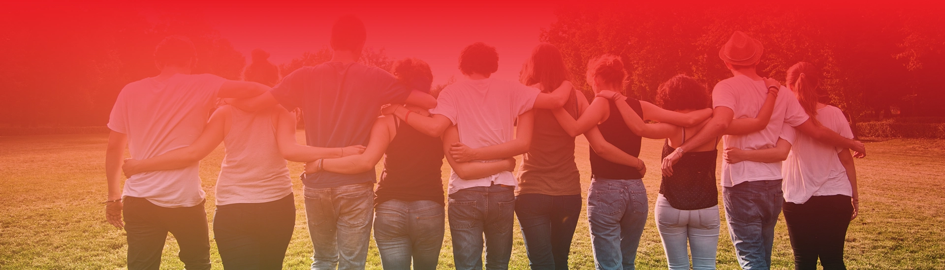 Grupa ludzi stoi na trawie obejmując się ramionami, widok od tyłu.