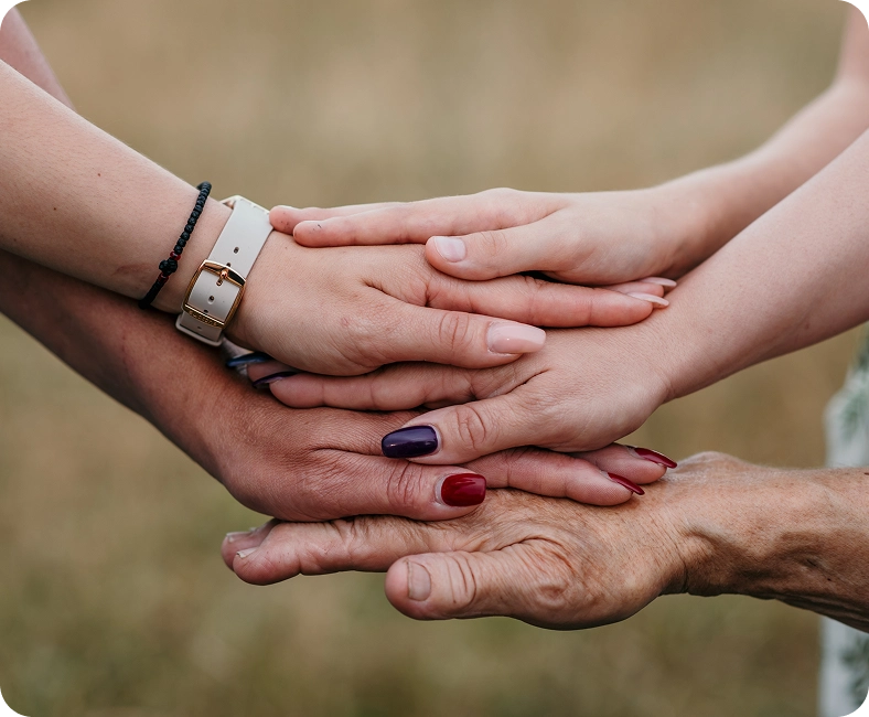 Cztery dłonie różnych osób położone jedna na drugiej, symbolizujące wsparcie i jedność.