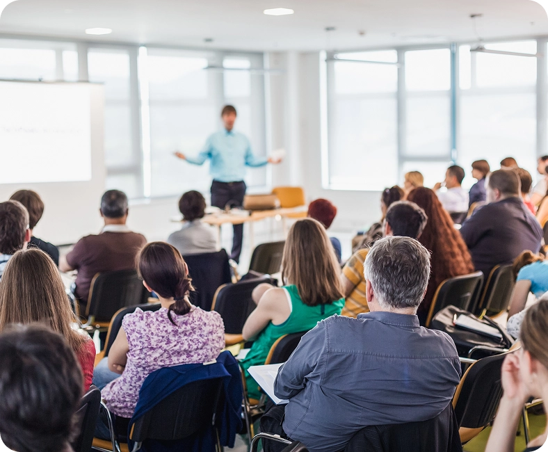 Mężczyzna prowadzi prezentację przed grupą słuchaczy w nowoczesnej sali konferencyjnej.